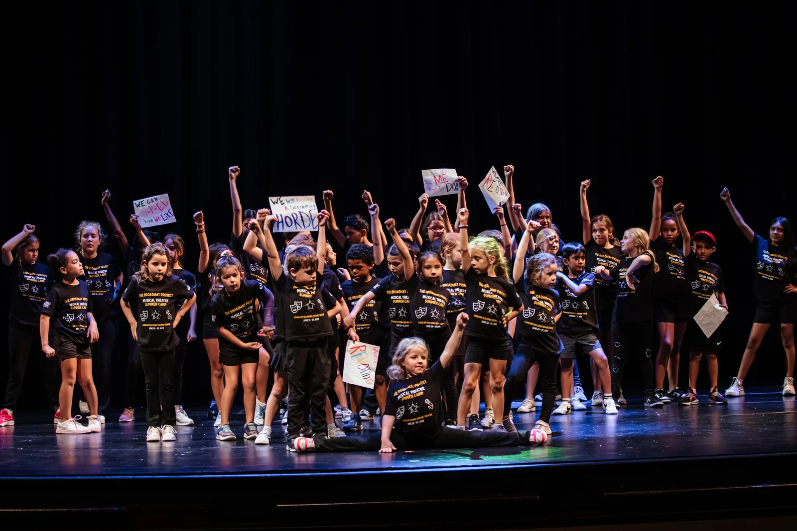 Campers onstage with fists raised holding signs