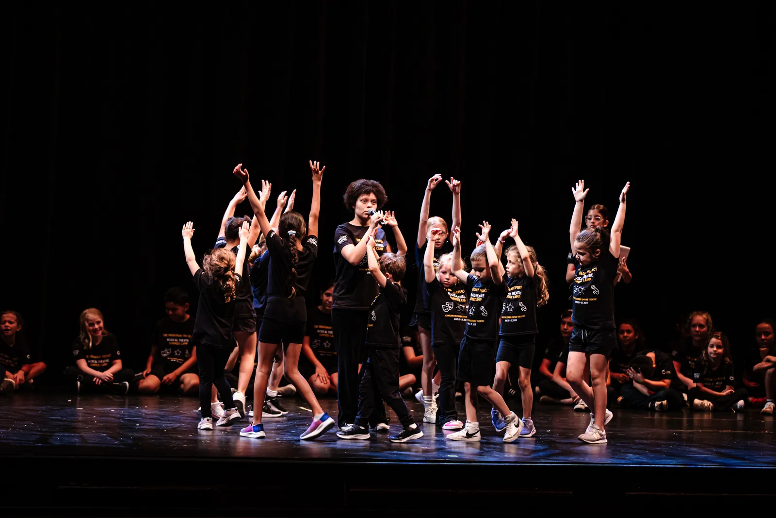 A group of campers dancing with arms raised onstage