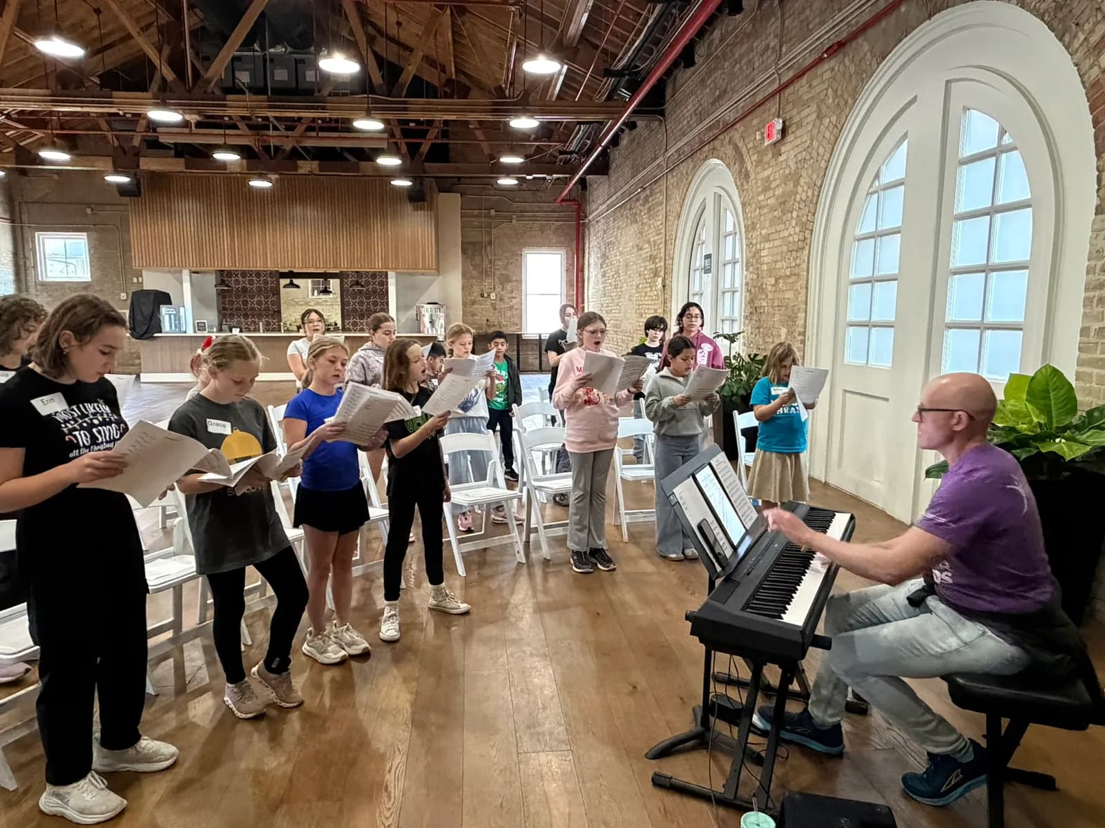Campers singing alongside a pianist in a rehearsal hall